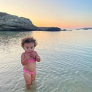 Aélys-Fleur a rejoint le concours — aidez-le/la à gagner de superbes lots ! beach, bikini, calm, child, curly_hair, cute, nature, outdoor, portrait, ripples, rocks, sand, sea, shallow_water, sky, summer, sunset, toddler, vacation, water