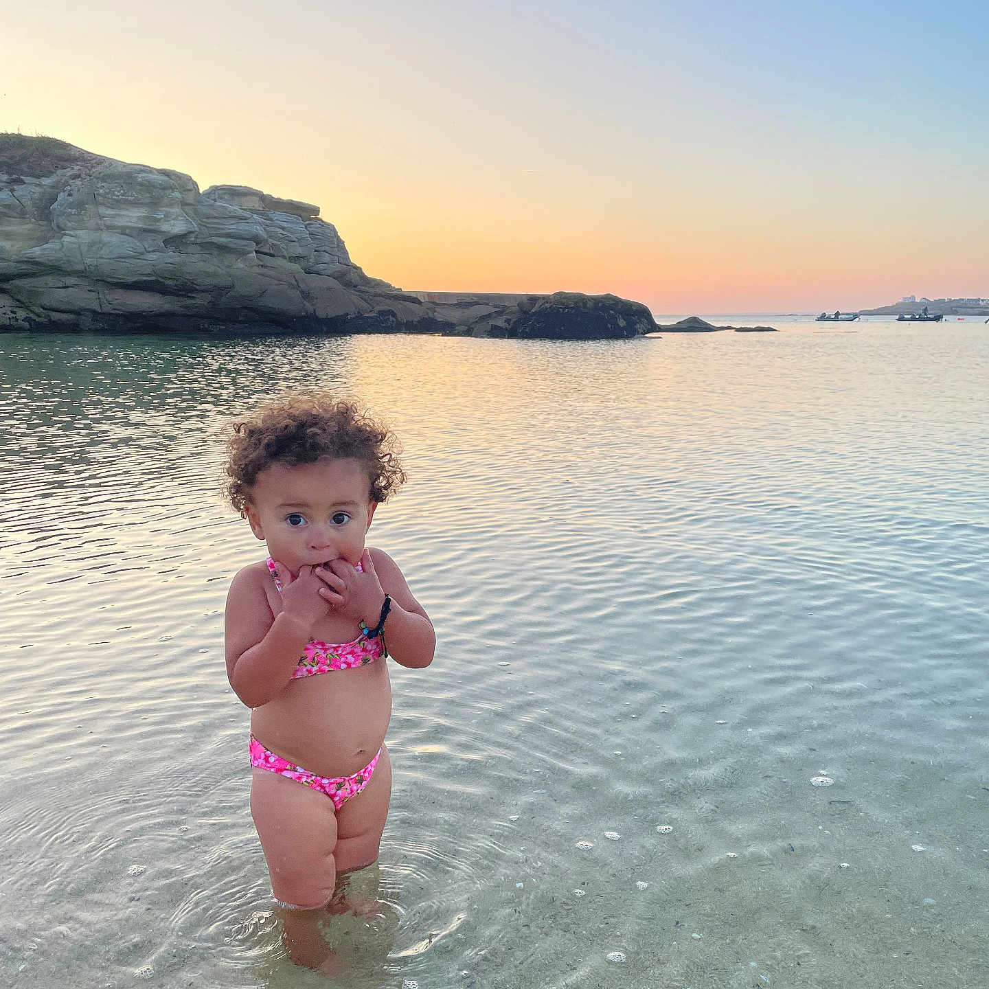 Aélys-Fleur a rejoint le concours — aidez-le/la à gagner de superbes lots ! beach, bikini, calm, child, curly_hair, cute, nature, outdoor, portrait, ripples, rocks, sand, sea, shallow_water, sky, summer, sunset, toddler, vacation, water