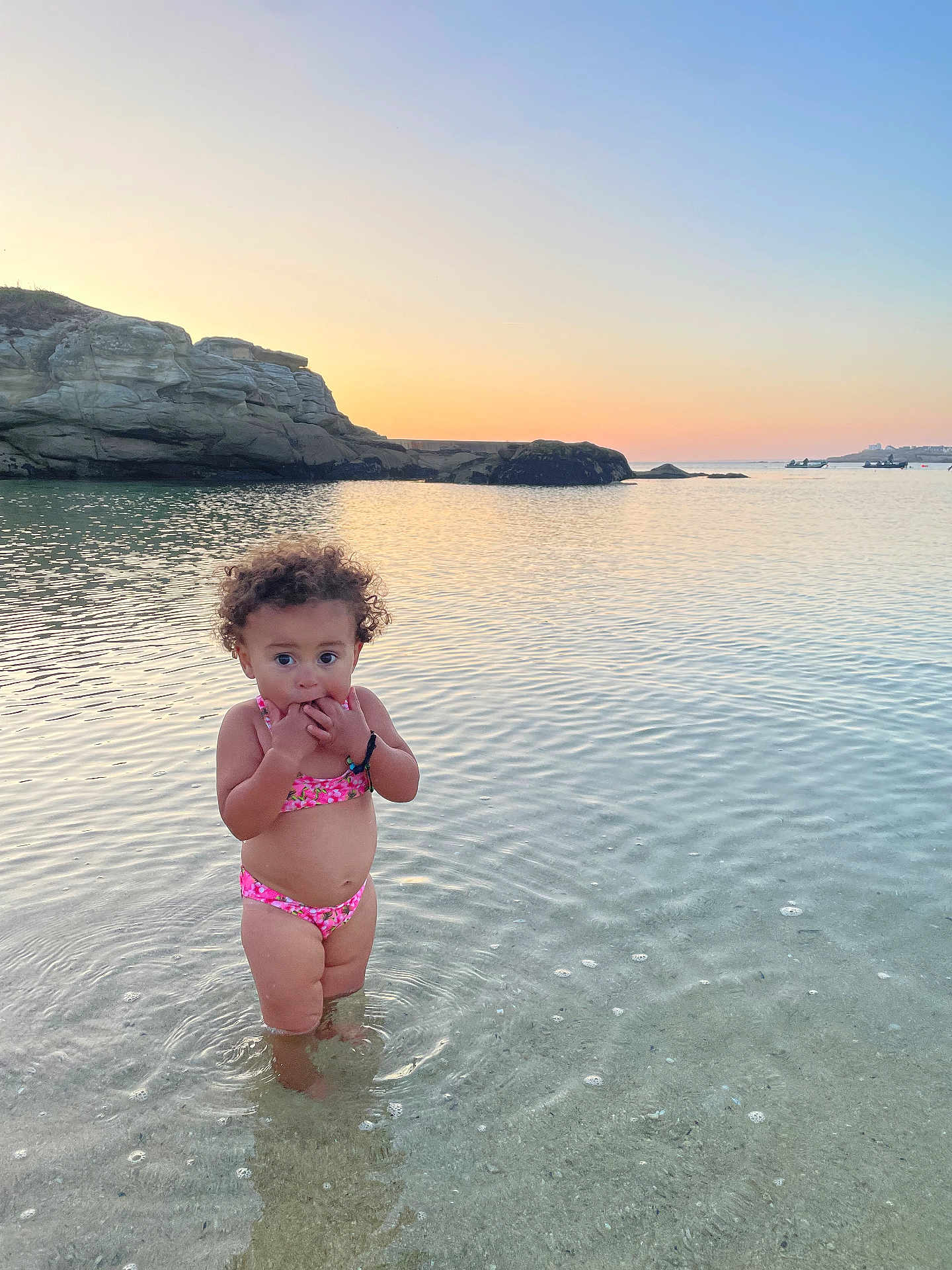 Aélys-Fleur a rejoint le concours — aidez-le/la à gagner de superbes lots ! beach, bikini, calm, child, curly_hair, cute, nature, outdoor, portrait, ripples, rocks, sand, sea, shallow_water, sky, summer, sunset, toddler, vacation, water
