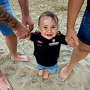 Tyméo participe au concours pour gagner de l'argent avec cette photo : adult, barefoot, beach, black_shirt, casual_clothing, child, denim_shorts, family, footwear_none, happy, holding_hands, outdoor, person, playing, sand, smile, summer, sunlight, tattoo, toddler