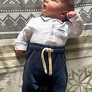 Léandro participe au concours pour gagner de l'argent avec cette photo : baby, infant, newborn, white_shirt, navy_pants, blanket, patterned_blanket, lying_down, curious, cute, small_hands, small_feet, indoors, soft_light, portrait, child, clothing, face, head, adorable
