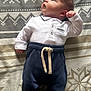 baby, infant, newborn, white_shirt, navy_pants, blanket, patterned_blanket, lying_down, curious, cute, small_hands, small_feet, indoors, soft_light, portrait, child, clothing, face, head, adorable