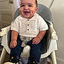 baby, child, high_chair, smiling, dimples, white_shirt, knitwear, blue_jeans, sneakers, indoor, happy, seatbelt, cute, portrait, young_child, furniture, person, hands, eyes, face