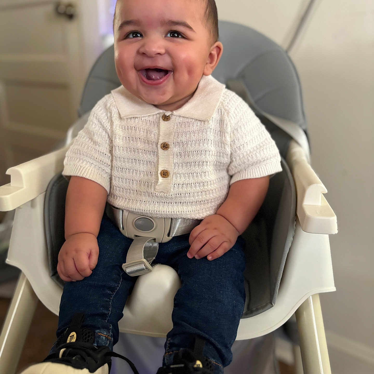 Trevell joined the competition — help win amazing prizes! baby, blue_jeans, child, cute, dimples, eyes, face, furniture, hands, happy, high_chair, indoor, knitwear, person, portrait, seatbelt, smiling, sneakers, white_shirt, young_child