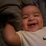 Trevell joined the competition — help win amazing prizes! baby, smiling, infant, child, blanket, white_shirt, logo, face, cheeks, arm, happy, lying_down, indoors, cute, person, skin, expression, closeup, toddler, cozy