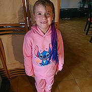 Elina a rejoint le concours — aidez-le/la à gagner de superbes lots ! child, girl, smile, purple_hair, braids, hoodie, pink_clothing, cartoon_print, indoor, floor_tiles, shoes, standing, happy, person, home, furniture, pants, casual, portrait, young