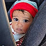 baby, child, car_seat, hat, straps, seatbelt, portrait, face, curious, wide_eyes, indoors, closeup, clothing, red, blue, young_child, infant, person, safety, transportation