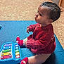 baby, child, toy, xylophone, red_sweater, socks, blue_mat, floor, indoor, cute, playing, knitted_clothing, colorful, infant, side_view, young_child, curious, seated, portrait, warm_lighting