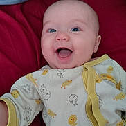 Isla is registered to the contest to win money with this photo: baby, infant, smiling, happy, onesie, duck_pattern, blue_eyes, lying_down, blanket, red_background, cute, child, apparel, young, face, expression, indoors, playful, person, cheerful