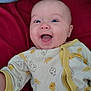 baby, infant, smiling, happy, onesie, duck_pattern, blue_eyes, lying_down, blanket, red_background, cute, child, apparel, young, face, expression, indoors, playful, person, cheerful