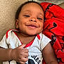 Major is registered to the contest to win money with this photo: baby, smile, face, hand, thumbs_up, mickey_mouse, shirt, red_blanket, carpet, child, cute, happy, lying_down, portrait, eyelashes, clothing, infant, indoors, person, toddler