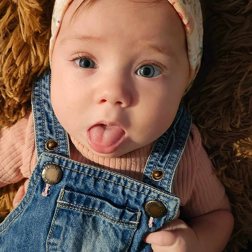 Clover joined the competition — help win amazing prizes! adorable, baby, blue_eyes, child, closeup, cute, denim_overalls, expression, face, fuzzy_rug, hands, headband, indoor, infant, pink_shirt, playful, portrait, skin, tongue_out, young_child