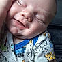 baby, sleeping, close_up, onesie, child, infant, smile, hand, face, cheek, clothing, cute, peaceful, resting, skin, person, young, indoors, comfort, doodle_print