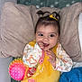 baby, blanket, child, colorful_ball, cushion, cute, face, happy, indoors, infant, lying_down, person, pigtails, pillow, pink_toy, playpen, smiling, soft_toys, toy, yellow_outfit