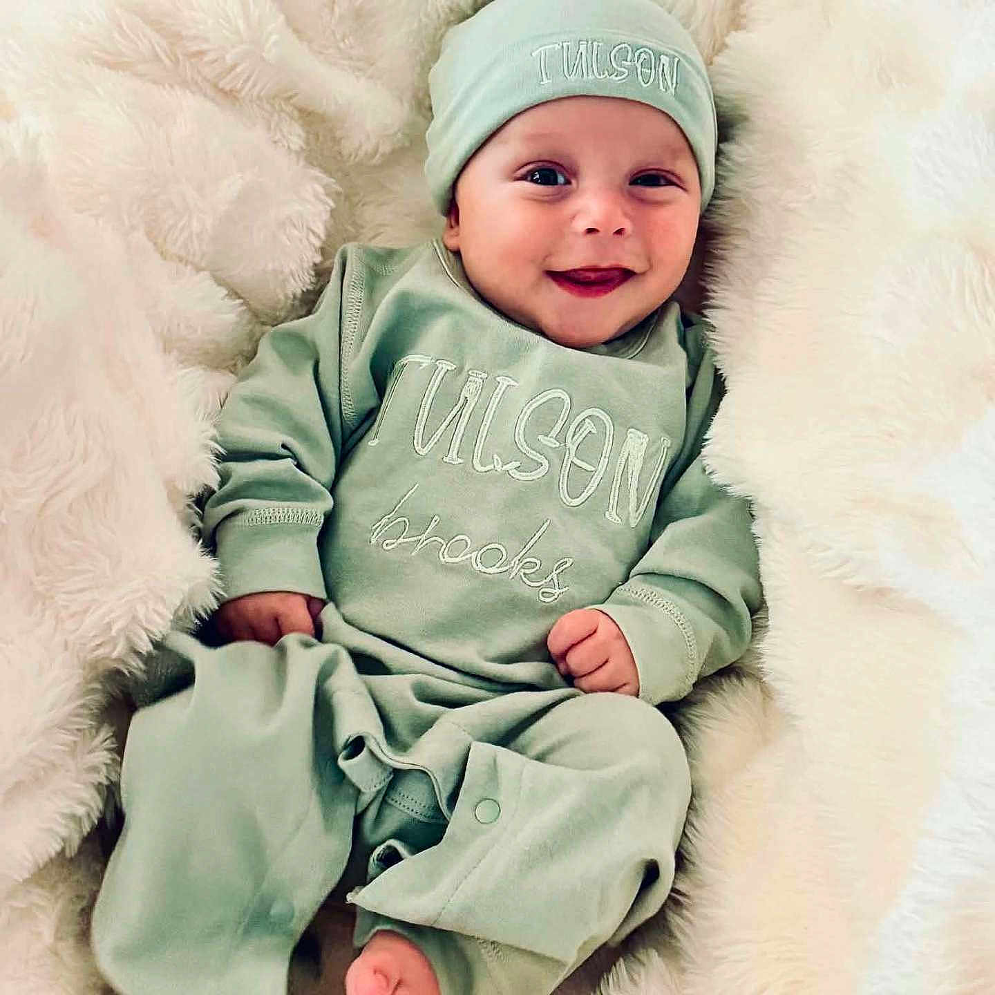 Tulson is registered to the contest to win money with this photo: baby, smiling, infant, pajamas, hat, blanket, soft, cozy, cute, lying_down, happy, child, newborn, face, foot, hand, indoors, portrait, apparel, sleepwear