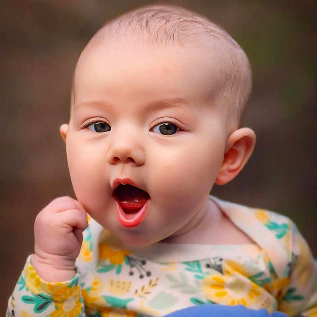 Cora joined the competition — help win amazing prizes! baby, infant, child, face, expression, mouth_open, clothing, floral_pattern, person, shoulder, holding, cute, portrait, skin, head, eyes, hand, outdoor, blurry_background, young