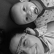 Ayden a rejoint le concours — aidez-le/la à gagner de superbes lots ! baby, adult, glasses, pacifier, pajamas, dinosaur_pattern, smile, face, portrait, closeup, black_and_white, lying_down, hand, eyewear, cozy, bonding, happy, infant, person, family