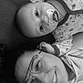 baby, adult, glasses, pacifier, pajamas, dinosaur_pattern, smile, face, portrait, closeup, black_and_white, lying_down, hand, eyewear, cozy, bonding, happy, infant, person, family