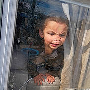 Everett is registered to the contest to win money with this photo: child, face, window, glass, dirty_window, curtain, hands, peeking, reflection, sunlight, expression, portrait, indoor, seat, sill, pressing_face, smiling, young_child, casual_clothing, sticker