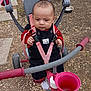 Eli Alexander is registered to the contest to win money with this photo: baby, child, tricycle, outdoor, playground, seat, straps, handlebars, footwear, ground, gravel, red, pink, black_clothing, expressionless, toy, vehicle, person, sitting, daylight