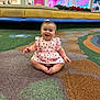 Allison is registered to the contest to win money with this photo: baby, child, smile, sitting, play_area, indoor, mall, bench, carpet, patterned_carpet, dress, heart_print, bow, happy, portrait, cute, toes, bright_colors, storefront, fun