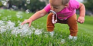 Xayna is registered to the contest to win money with this photo: toddler, child, grass, outdoor, bubbles, pacifier, pink_shirt, brown_pants, white_shoes, green_lawn, nature, daylight, curious, playing, baby, person, young_child, hair_tied, exploring, park