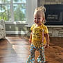 Xayna is registered to the contest to win money with this photo: toddler, child, indoor, yellow_shirt, fringe_top, taco_print, pants, bell_bottoms, standing, smiling, bracelet, hair_tied, wooden_floor, natural_light, window, living_room, fireplace, cute, happy, fashion