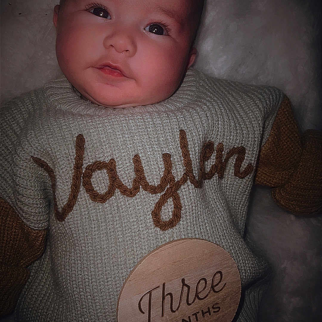 Vaylen-Stone is registered to the contest to win money with this photo: baby, calm, child, cozy, cute, diaper, face, indoors, infant, knitted_clothing, lying_down, name_embroidery, newborn, person, portrait, sleepy, soft_blanket, sweater, three_months, young_child