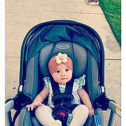 Sinéad joined the competition — help win amazing prizes! baby, car_seat, stroller, child, infant, flower_headband, white_tights, floral_outfit, sidewalk, grass, outdoor, cute, sitting, seat_belt, gray, person, young_child, headwear, wide_eyes, curious