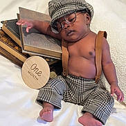 Legend is registered to the contest to win money with this photo: baby, bare_chest, books, cap, cozy, cute, foot, glasses, hand, houndstooth, indoors, infant, one_month, pants, portrait, relaxed, sleeping, soft_fabric, suspenders, wooden_sign