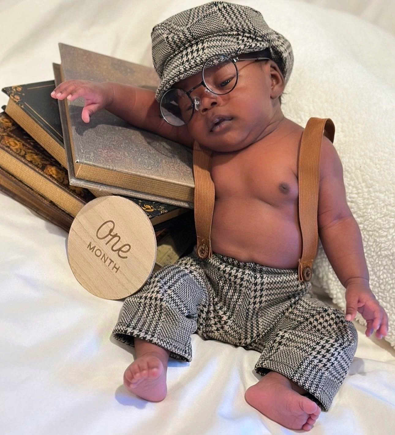 Legend is registered to the contest to win money with this photo: baby, bare_chest, books, cap, cozy, cute, foot, glasses, hand, houndstooth, indoors, infant, one_month, pants, portrait, relaxed, sleeping, soft_fabric, suspenders, wooden_sign