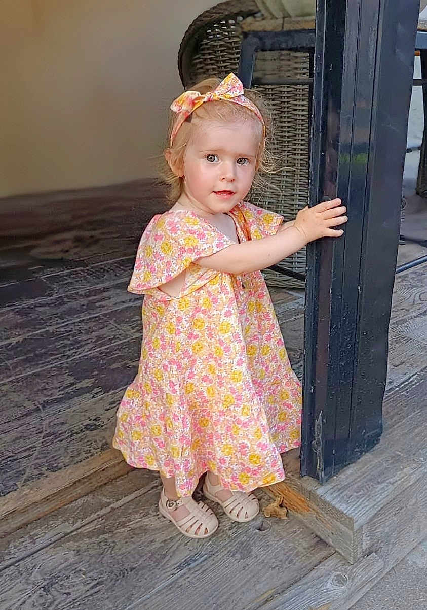 Ambre a rejoint le concours — aidez-le/la à gagner de superbes lots ! child, toddler, girl, floral_dress, headband, shoes, wooden_floor, post, hand, curly_hair, pink, yellow, pattern, standing, indoor, portrait, cute, small, person, summer