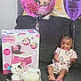 balloon, birthday_cake, celebration, child, clothing, couch, face, feet, gift_box, hair, happy, indoors, minnie_mouse, party, person, pink, purple, smiling, toddler, toy