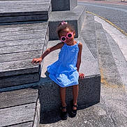 Maya participe au concours pour gagner de l'argent avec cette photo : child, girl, sunglasses, blue_dress, steps, concrete, wooden_platform, outdoor, sunny, daylight, sky, clouds, waterfront, cityscape, footwear, black_shoes, smiling, fashion, portrait, casual