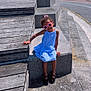 child, girl, sunglasses, blue_dress, steps, concrete, wooden_platform, outdoor, sunny, daylight, sky, clouds, waterfront, cityscape, footwear, black_shoes, smiling, fashion, portrait, casual
