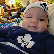 Seviin is registered to the contest to win money with this photo: baby, infant, face, child, hat, clothing, sweater, indoor, living_room, toy, person, blur, couch, plant, furniture, casual, portrait, cute, maple_leaf, relaxation