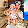 woman, baby, child, tattoo, headscarf, blue_cap, paintbrush, apron, smile, indoor, painting, art, happy, person, holding, furniture, couch, floor, portrait, home