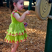 Chloe joined the competition — help win amazing prizes! toddler, child, playground, green_dress, pineapple_pattern, wood_chips, outdoor, curious, shoes, socks, summer, play_equipment, nature, side_view, young_child, person, daylight, fun, exploration, casual_clothing