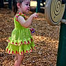 toddler, child, playground, green_dress, pineapple_pattern, wood_chips, outdoor, curious, shoes, socks, summer, play_equipment, nature, side_view, young_child, person, daylight, fun, exploration, casual_clothing