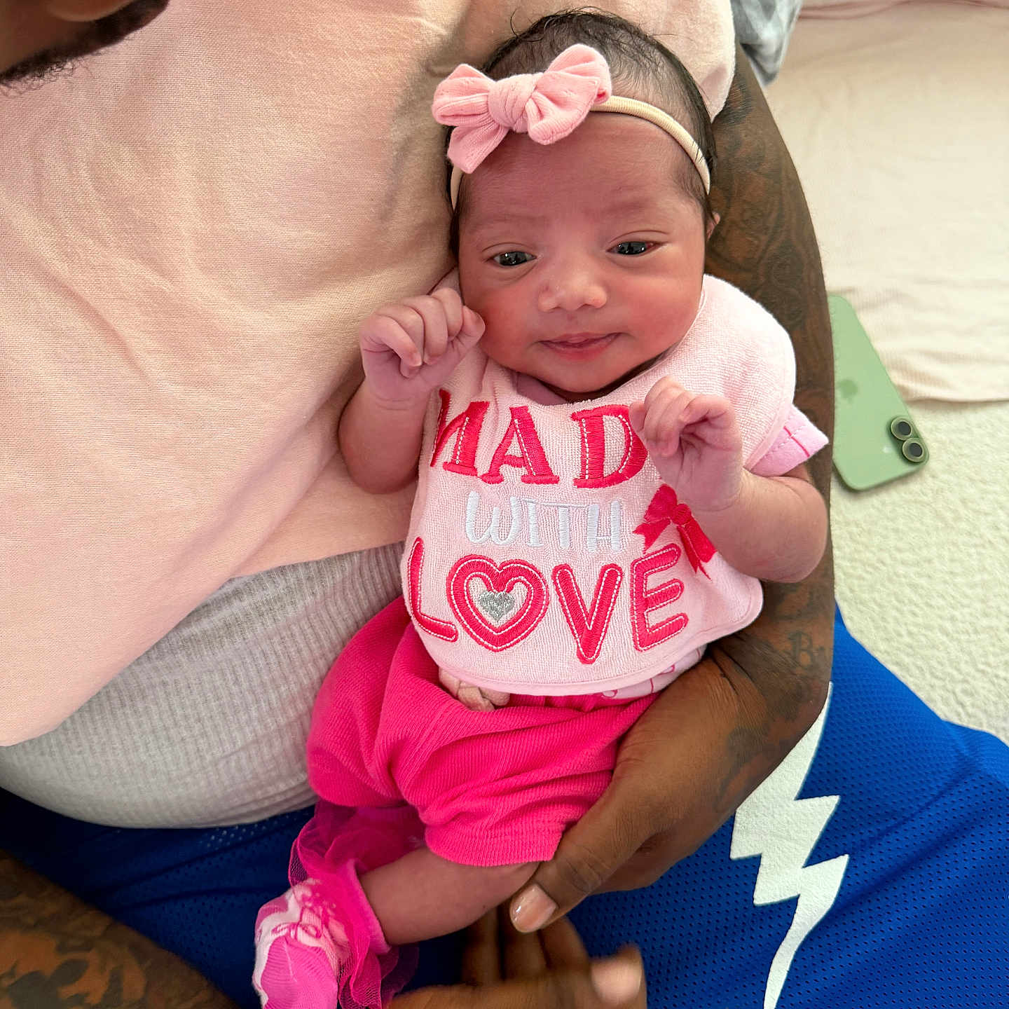 Milan joined the competition — help win amazing prizes! baby, newborn, infant, pink_clothing, headband, bow, bib, tattooed_arms, holding, portrait, happy, cute, indoor, soft_light, person, human, child, love, cozy, family