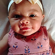 Jayla is registered to the contest to win money with this photo: baby, child, face, headband, bow, dress, pink, floral_pattern, smile, portrait, cute, infant, person, lying_down, indoors, soft_lighting, skin, eyes, cheeks, young