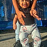 toddler, child, smiling, happy, outdoor, playground, adult, arms, lifting, portrait, face, black_shirt, patterned_pants, sneakers, blue_bench, sunlight, park, play, standing, family