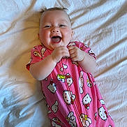 Madison is registered to the contest to win money with this photo: baby, smiling, pink_onesie, cartoon_print, bed, white_bedspread, happy, child, infant, clapping_hands, cute, sleepwear, indoor, person, portrait, joyful, playful, young, head, face