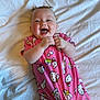 baby, smiling, pink_onesie, cartoon_print, bed, white_bedspread, happy, child, infant, clapping_hands, cute, sleepwear, indoor, person, portrait, joyful, playful, young, head, face