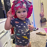 Athena joined the competition — help win amazing prizes! toddler, child, indoor, carpet, bonnet, dinosaur_shirt, diaper, footwear, slippers, bag, speaker, drawer, wall, person, clothing, toy, furniture, room, floor, portrait