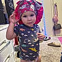 toddler, child, indoor, carpet, bonnet, dinosaur_shirt, diaper, footwear, slippers, bag, speaker, drawer, wall, person, clothing, toy, furniture, room, floor, portrait