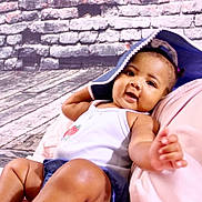 Naziya joined the competition — help win amazing prizes! baby, child, smiling, hat, blue_hat, white_tank_top, denim_shorts, brick_wall, wooden_floor, indoor, cute, happy, reaching_hand, portrait, infant, playful, relaxed, skin, person, clothing