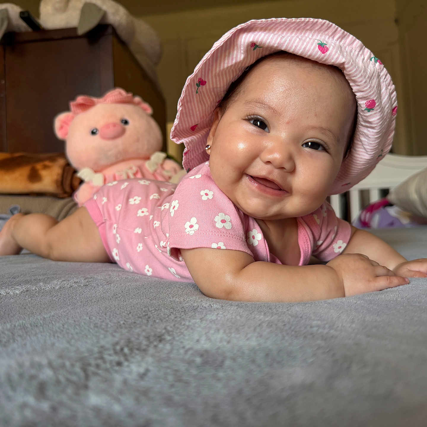 Alahia joined the competition — help win amazing prizes! baby, smiling, pink_hat, onesie, stuffed_toy, pig_toy, bed, blanket, pillow, indoor, child, cute, happy, face, headwear, lying_down, infant, soft_toy, room, portrait