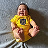 adorable, baby, blanket, child, clothing, cute, face, feet, happy, head, indoor, infant, lying_down, person, playful, skin, small_feet, smiling, texture, yellow_onesie