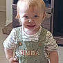toddler, child, smiling, indoor, overalls, light_hair, blue_eyes, striped_shirt, furniture, cabinet, wooden, floor, cute, happy, person, portrait, clothing, baby, standing, young_child